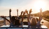 Back view of happy friends driving cabriolet with raised hands