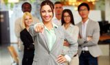 Smiling handsome businesswoman with team in office pointing finger at you